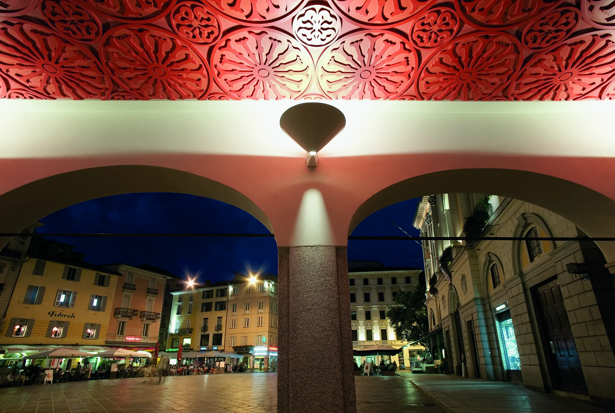 Portico con soffitto decorato rosso affacciato su una piazza di sera